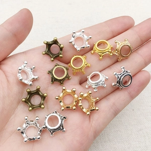 Close-up of alloy crown charms in gold, silver, and bronze held in hand for DIY jewelry