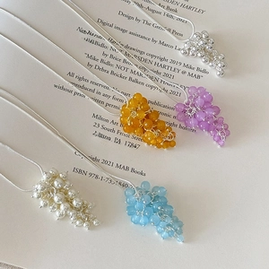 Dettaglio delle collane a grappolo d'uva in cinque colori su sfondo di un libro