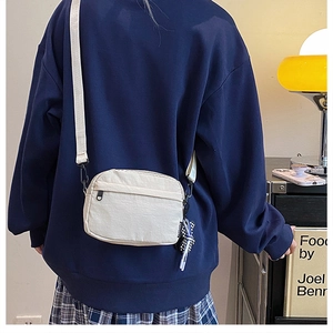 Sac bandoulière en nylon blanc cassé porté avec un sweat à capuche bleu marine décontracté