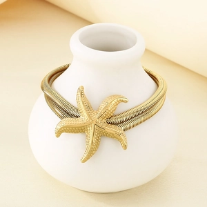 Close-up of golden flat snake chain necklace with starfish pendant on ceramic vase