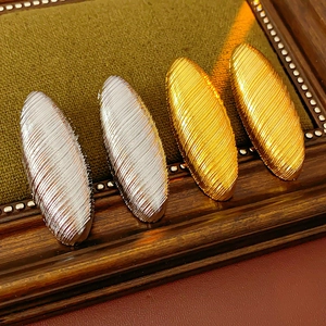Macro detail of textured oval metal earrings in gold and silver finish on a green display