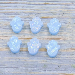 Blue opal Hamsa palm charms with iridescent flakes on light wood background