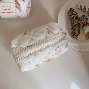 Macro detail of quilted cream makeup bag with floral dog print and sturdy white zipper