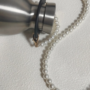 Detail of white pearl chain with gold lobster clasp and black rubber loop connector