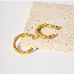 Detailed close-up of gold-plated twisted rope hoop earrings on a beige stone base