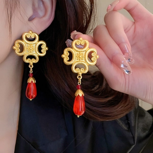 Detail of vintage gold earrings with red teardrop pendants and ornate hollow metal patterns