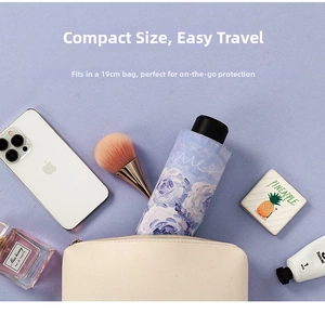 Compact folding sun umbrella with purple rose print next to makeup and a phone