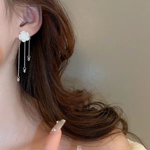 Détail de boucles d'oreilles à pompons avec camélia blanc sur un modèle de profil