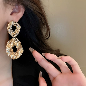 Close-up of golden geometric earrings with hammered texture on a model side profile