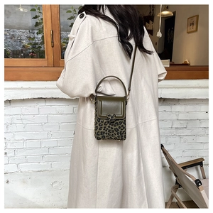 Detail of olive green and leopard print mini crossbody bag styled with a beige coat