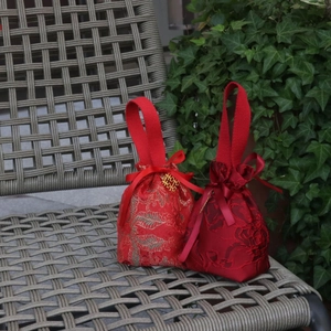 Detail of red brocade wedding candy bags with silk handles and golden charm on a chair