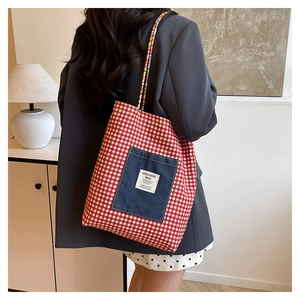 Détail du sac cabas en toile à carreaux rouges avec poche en denim porté par un mannequin