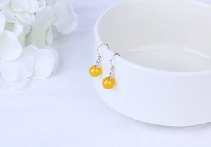Detailed macro view of yellow agate bead earrings hanging on a white ceramic bowl edge