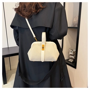 Modern white shell crossbody bag with metal clasp worn over a black wool coat