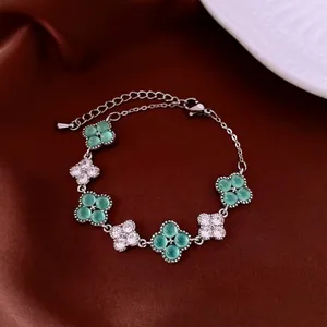 Elegant four-leaf clover bracelet with green gemstone and zircons on silk background