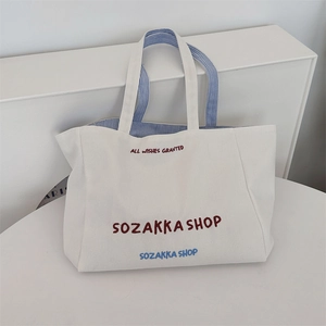 Detailaufnahme einer weißen Segeltuch-Tasche mit roter Stickerei und gestreiftem Innenfutter