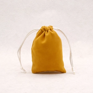 Detail of a small golden velvet drawstring jewelry pouch on a textured background