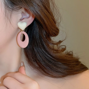 Close-up of white resin heart and pink oval hoop earrings worn by a model