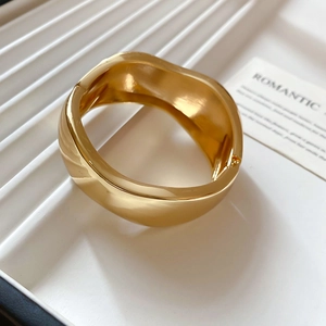 Detailed close-up of wide golden wave bangle showing polished finish and organic fluid design