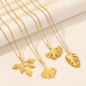 Detailed view of 18K gold ginkgo and monstera leaf pendants on soft textured fabric