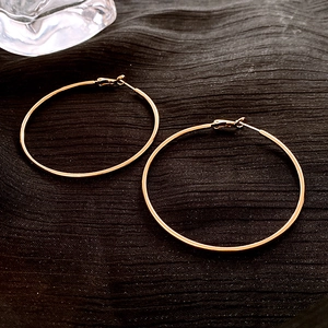 Detail shot of large thin gold hoop earrings on dark textured fabric background