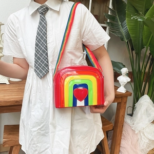 Detail of glossy rainbow crossbody bag with red heart applique and wide woven strap