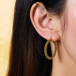 Gros plan de créoles dorées à texture tressée portées à l'oreille d'un modèle