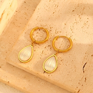 Detail view of 18k gold earrings with teardrop white shell pendants on textured stone