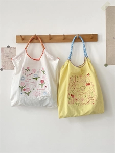 Detail of embroidered tote bags with plaid handles and artistic floral patterns