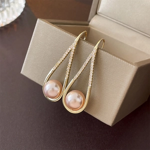 Detail of gold teardrop earrings with pink pearls and crystals on a beige jewelry box