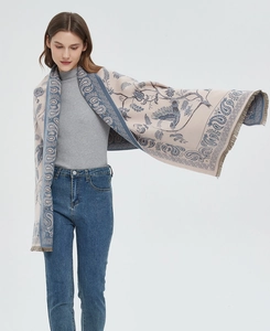 Detail of soft beige scarf with blue paisley pattern and fringe edges worn by a model