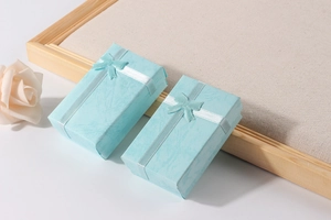 Close-up of two blue paper jewelry boxes featuring decorative ribbon bows and white rose