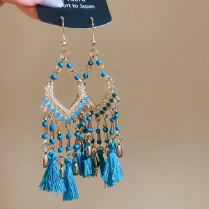 Detail of gold flower earrings with blue beads and flowing tassels held by hand