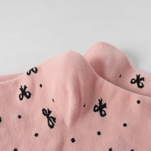 Macro shot of pink cotton socks featuring black bow patterns and fine knit texture