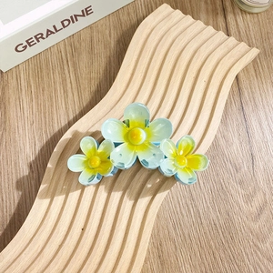 Three-flower claw clip with gradient blue-green petals and yellow stamens on wood