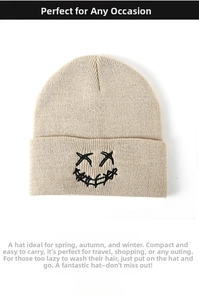 Close-up of beige knit beanie with black cross-eye smiley face embroidery detail