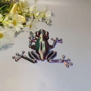 Top view of a 3D printed iridescent articulated frog toy on a grey surface with white flowers