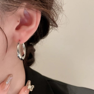 Close-up of sleek silver C-shaped metal hoop earrings worn to show mirror-like finish