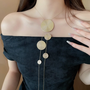 Detail view of gold geometric round textured tassel necklace on a black dress
