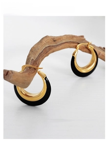 Detailed shot of black and gold enamel hoop earrings hanging on an artistic wooden branch
