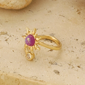 Elegante anello sole dorato con gemma viola su superficie in pietra, gioielli moda