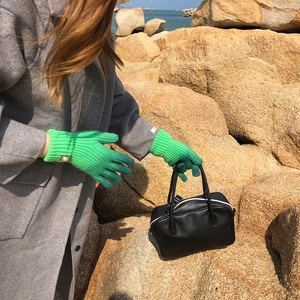 Close-up of green knitted gloves held with a black leather bag against a coastal backdrop