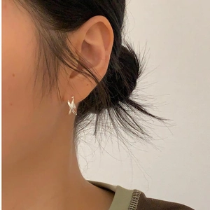 Close-up of minimalist sterling silver cross hoop earrings on woman ear lobe