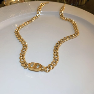 Detailed macro view of the gold-tone thick curb chain and CD logo pendant on a white plate