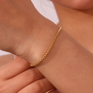 Detailed view of an 18K gold plated box chain bracelet worn on a woman's wrist