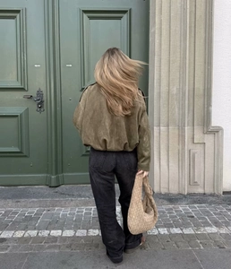 Close-up of olive green suede bomber jacket with premium texture and woven leather handbag