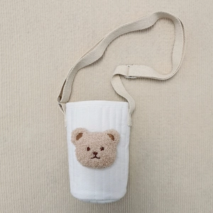 Close-up of quilted white cotton water bottle bag with brown bear embroidery and strap