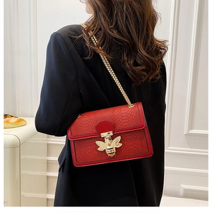 Close-up of red snake-embossed crossbody bag with a golden bee clasp detail