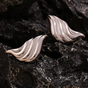 Macro detail of silver liquid drop earrings with textured waves on a dark stone surface