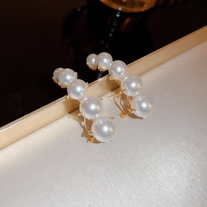 Gold-plated C-shaped earrings with graduated white pearls on a metallic tray